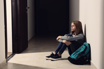 Sad teenage girl sitting on floor indoors