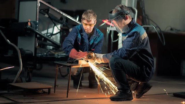 Workers wearing mask cuts metal with hand disc grinder abrasive saw
