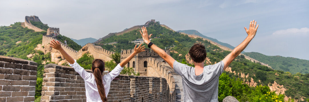 China travel people winning of joy in Asia on Great Wall, Beijing, chinese landmark. Young couple tourists with arms up in happiness winners visiting Great Wall panorama landscape crop for background.