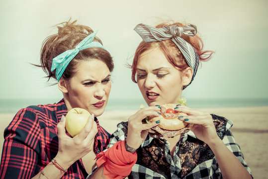 healthy diet vs junk food concept. two girls eating different foods together looking disgusted at junk food.
