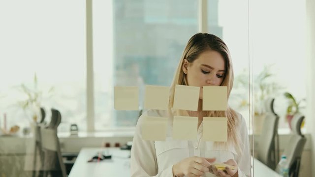 young businesswoman sticking sticky notes on glass at office