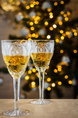 Two crystal glasses with wine near beautiful christmas tree and blurred lights