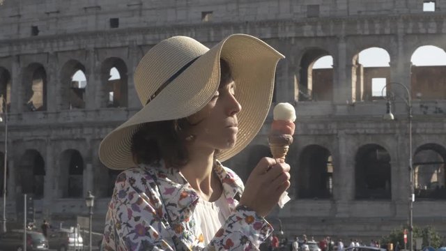 Beautiful young woman in colorful fashion dress eating ice cream in front of colosseum in Rome at sunset attractive girl with elegant straw hat FLAT NO GRADING