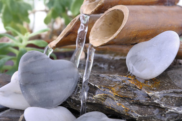 water flowing from littte bamboo fountain on pebble in heart shape 
