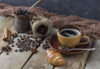 on a wooden table a coffee grinder, a cup of coffee, a grain of coffee and a croissant