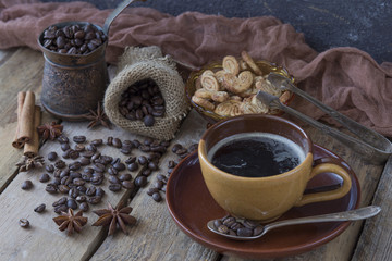 on a wooden table a coffee grinder, a cup of coffee, grains of coffee and biscuits