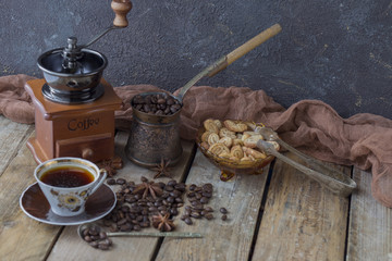 on a wooden table a coffee grinder, a Turk, a cup of coffee, a grain of coffee and biscuits in a vase