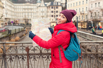 A happy woman on the bank of the Tepla river in Karlovy Vary looking at a map and tries to find a tourist attraction