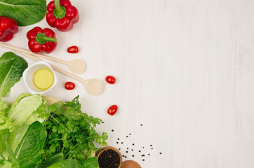Cooking fresh spring salad of green and red vegetables, spices on white wooden background, border, top view.