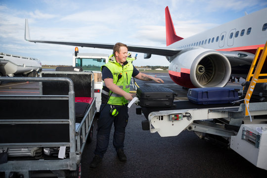 Worker Arranging Luggage On Trailer Connected To Airplane