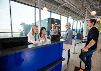 Staff Using Computer While Passengers Waiting In Airport