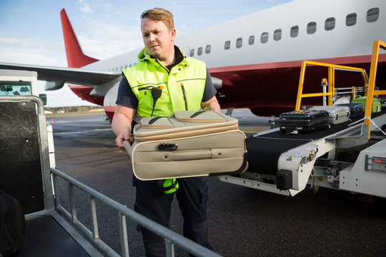 Worker Placing Luggage In Trailer Against Airplane