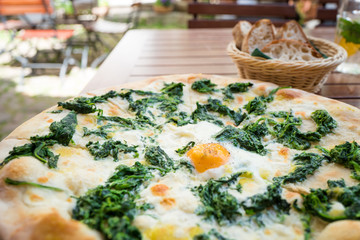 Spinach pizza with egg in a garden restaurant outside