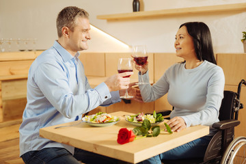 Drinking wine. Attractive alert blond man and a beautiful inspired handicapped woman smiling and drinking wine and having dinner