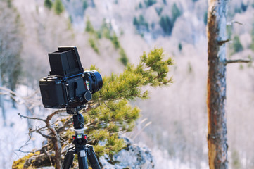 Retro professional camera on a tripod, outdoor wildlife photography. Mountains, forest background.