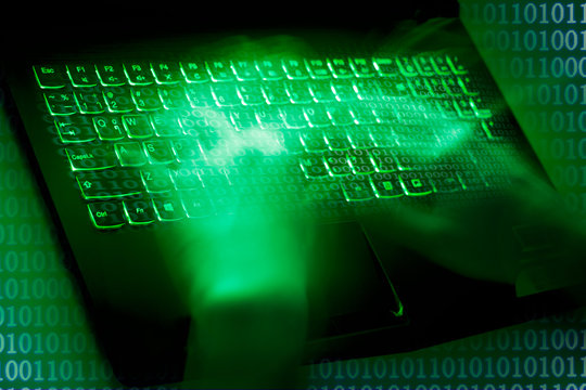 A computer programmer or hacker prints a code on a laptop keyboard to break into a secret organization system.