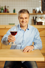 Join me. Attractive alert well-built man drinking wine and wearing a blue shirt while relaxing