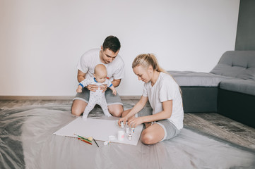 happy young family with beautiful little infant child painting together on floor at home