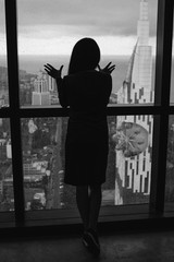 Girl stands with his back near the window of a tall building