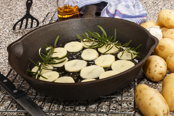 sliced potato with rosemary in a cast iron pan