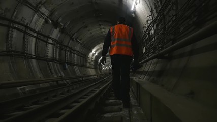 Man goes along the railway tracks in subway tunnel - Powered by Adobe