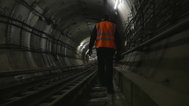 Man goes along the railway tracks in subway tunnel