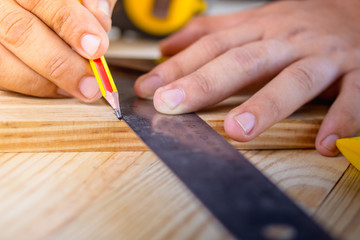 The carpenter uses a pencil on the wooden board in workshop.