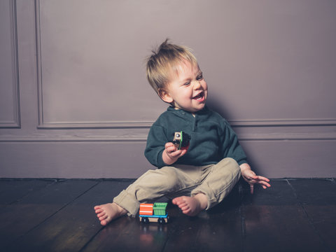Grimacing little boy playing with wooden train