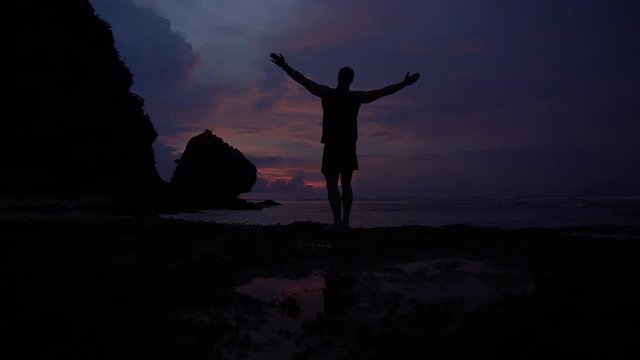 Beautiful sunset above ocean, young man rising hands into air
