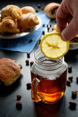 man's hand putting lemon slice in jar cup filled with black tea, buisquits on back front