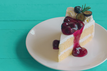 Blueberry cream cake on white plate on blue wood table in top view. Vanilla sponge cake decorated with dairy whipped cream and blueberry sauce so soft sweet and delicious. Homemade bakery concept.