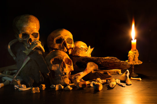 Pile of skulls on pile bone and old timber with has candle light bright splash in dark room