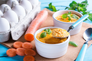 Spoon and casserole with tasty carrot souffle on wooden table