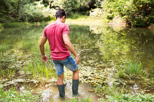 Teenage boy in rubber boots standing in lake.