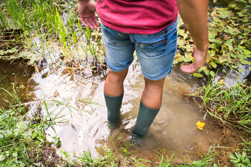 Teenage boy in rubber boots standing in lake.