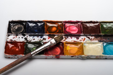 Watercolor multicolored paints and brushes for drawing lie on a blank sheet of paper on a white background