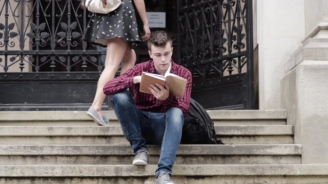 Handsome man sitting on steps and reading a book 