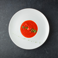Tomato soup with spices and fresh basil in a white plate on a black concrete background. Useful dietary snack and lunch. Place for text. Flat lay, top view. Isolated.