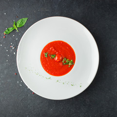 Tomato soup with spices and fresh basil in a white plate on a black concrete background. Useful dietary snack and lunch. Place for text. Flat lay, top view. Isolated.