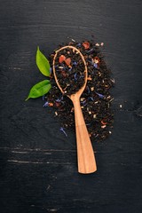 Black tea with flower petals of cornflower and dry berries. On a wooden background. Top view. Copy space.