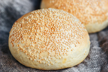 Round bun, sesame bun, bread rolls. Tasty burger bread with sesame on wooden, burlap background. Freshly baked hamburger buns. Top view.