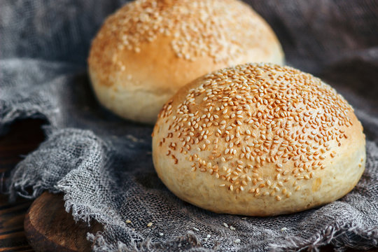 Round bun, sesame bun, bread rolls. Tasty burger bread with sesame on wooden, burlap background. Freshly baked hamburger buns. Top view.