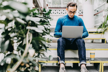 Young and attractive artist, looking for inspiration to write his new book. Using your laptop in a quiet greenhouse while having a coffee. Lifestyle..