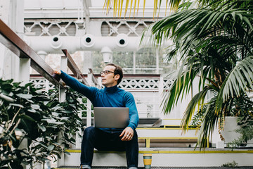 Young and attractive artist, looking for inspiration to write his new book. Using your laptop in a quiet greenhouse while having a coffee. Lifestyle..