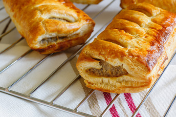 Freshly baked sausage rolls made with puff pastry fresh out of the oven cooling on a cooking trivet