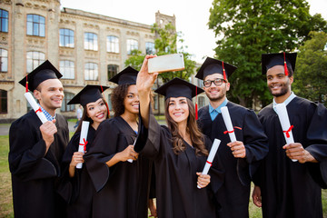 Memories of six international cheerful graduates, posing for shot, attractive brunette lady is taking, wearing gowns and mortar boards, outside on a summer day, so excited and gathered
