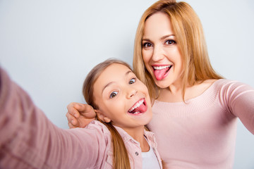 Self portrait of crazy, foolish mother and doughter showing tongue out, kid making selfie on mobile phone over grey background, spending weekend, woman's day together