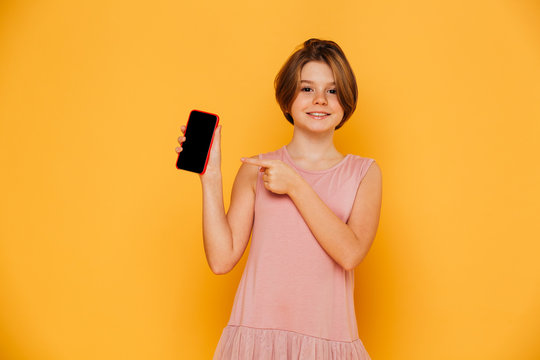 Smiling girl pointing at blank screen of smartphone isolated