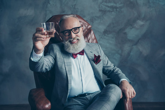 Portrait Of Bearded, Lucky, Old Rich Man In Formal Wear With Bow Tie And Pocket Square, Sitting On Chair, Holding, Raise Glass With Whiskey,  Crypto-currency, Shares, Stock