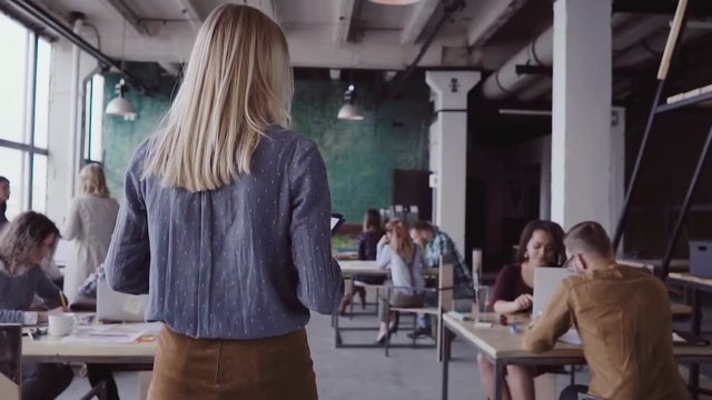 Female blonde team leader walking through office and controls work of employee. Female looks the fabric examples